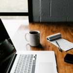 MacBook Pro, white ceramic mug,and black smartphone on table